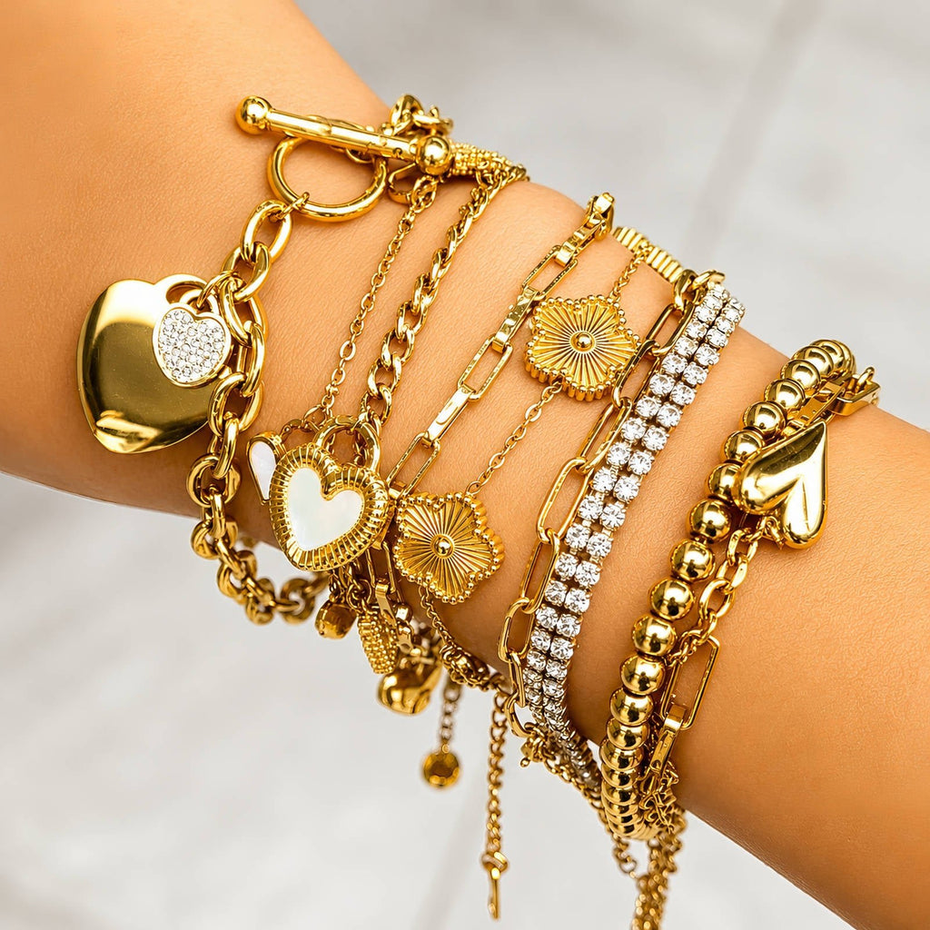 Goldfarbenes Tennisarmband mit Strassstreifen und mehreren Anhängern am Handgelenk.