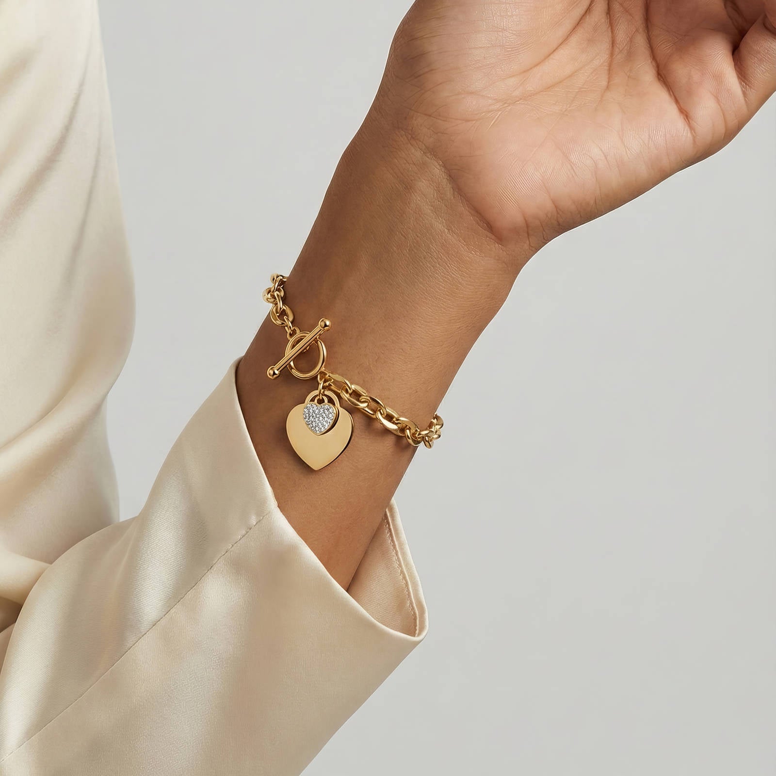 Goldfarbenes Armband am Handgelenk mit Herzplatte und Kettenanhängern