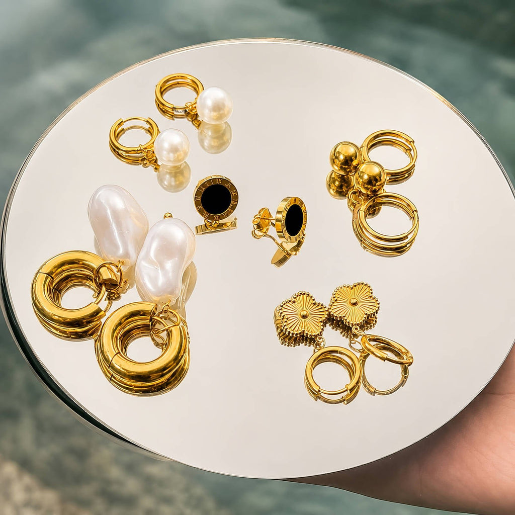 Mehrere goldfarbene Ohrringe auf Tablett, teils mit Perlen und schwarzem Stein
