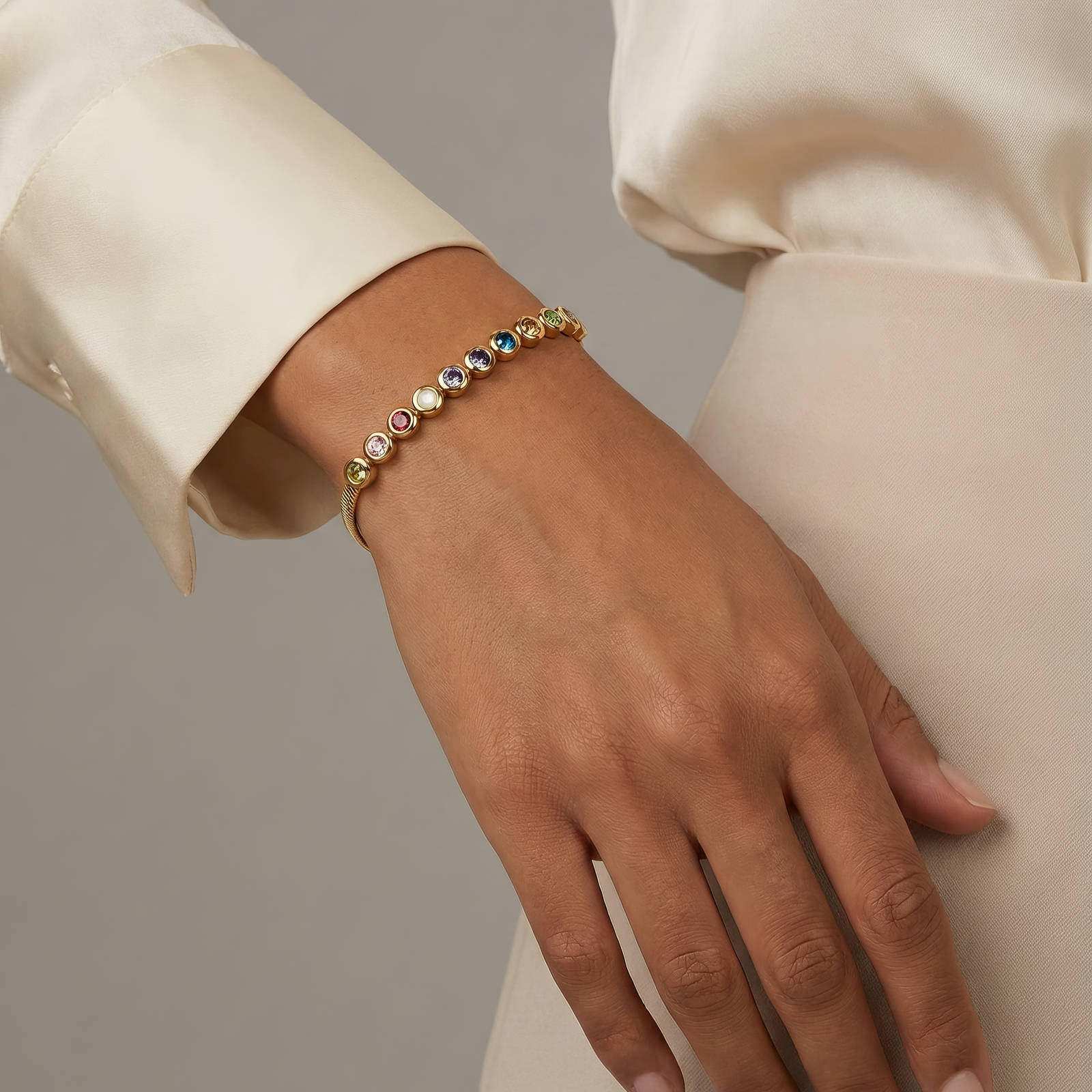 Armband am Handgelenk mit kleinen bunten Steinchen auf goldfarbenem Band