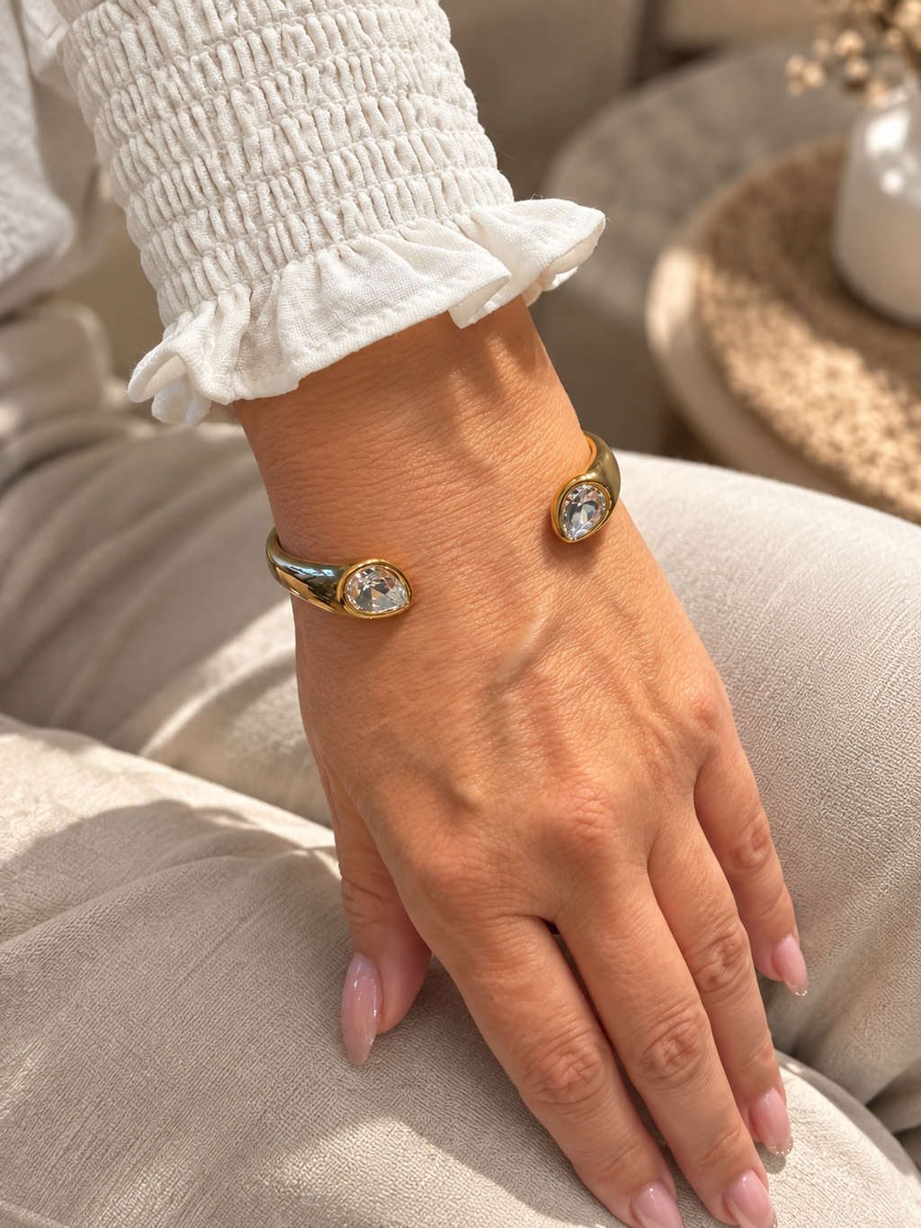 Armreif Larme in Gold am Handgelenk, getragen zu einer weißen Bluse mit Rüschenmanschette